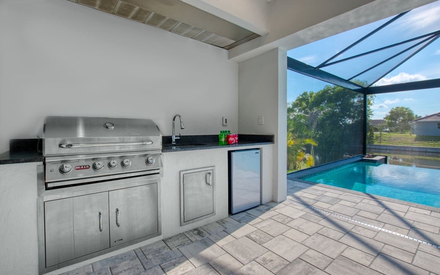 Una cocina exterior moderna con una parrilla de acero inoxidable, un refrigerador y un lavamanos integrado.