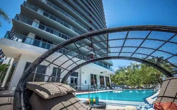 A modern hotel with a pool area, including lounge chairs and a glass-enclosed structure.