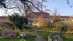 A garden with a bench, a stone sculpture, and a path leading to a house with a red-tiled roof. - Le Clos des Pommes (Bioncourt)