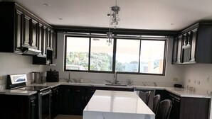 A modern kitchen with dark cabinetry, a large marble island, and a window providing a view of greenery outside. - Luxury Villa, 20 minutes from SJO airport , Gated community (Provincia de Alajuela)