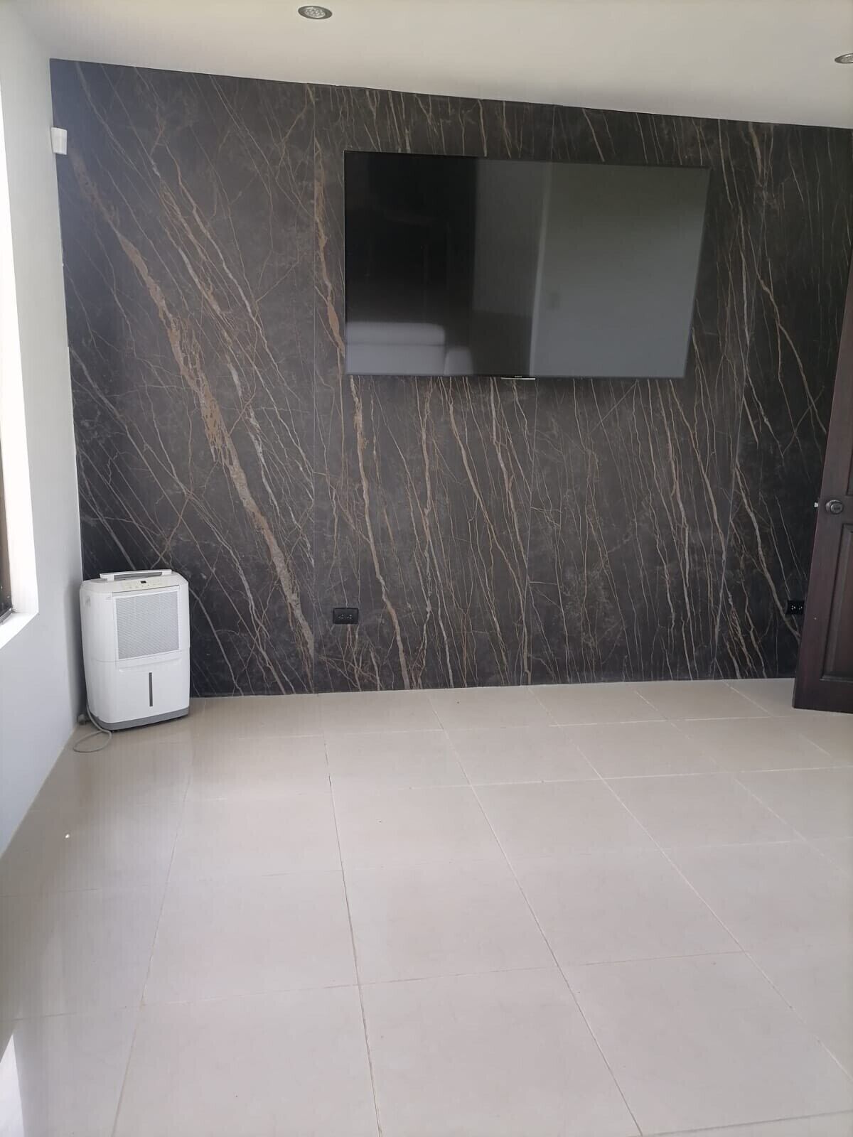Habitación con pared de diseño de mármol, televisor de pantalla plana montado y enfriador de aire portátil.