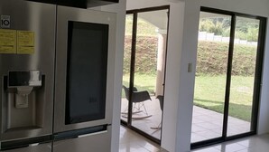 A modern kitchen with a stainless steel refrigerator, a built-in water dispenser, and a sliding glass door leading to an outdoor patio with chairs. - Luxury Villa, 20 minutes from SJO airport , Gated community (Provincia de Alajuela)