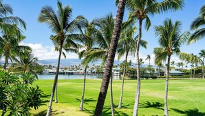 Un campo de golf con palmeras y vistas a un cuerpo de agua y edificios al fondo.