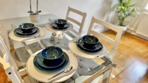 Una mesa de comedor con cubierta de vidrio, rodeada de sillas, y una planta decorativa al fondo.