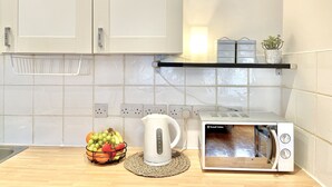 Una cocina con armarios blancos, microondas, hervidor y una cesta de frutas sobre la encimera.
