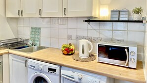 Una cocina con armarios blancos, lavadora, microondas y un frutero en la encimera.