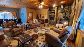 A cozy living room with leather sofas, a fireplace, and a stone wall. - Pinetree Cabin - 4 king beds, stunning views (Custer)