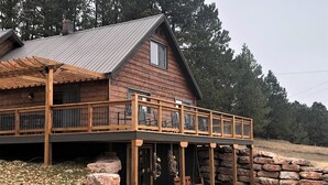 A wooden cabin with a balcony, stone foundation, and outdoor seating area. - Pinetree Cabin - 4 king beds, stunning views (Custer)