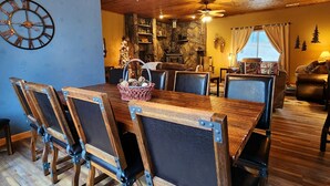 A rustic dining area with a wooden table and chairs, a stone wall, and a fireplace. - Pinetree Cabin - 4 king beds, stunning views (Custer)