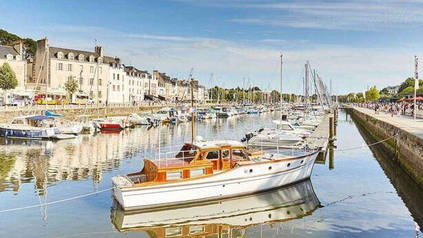 Un port de plaisance avec des bateaux amarrés le long de la rive, des bâtiments en arrière-plan et un ciel dégagé.