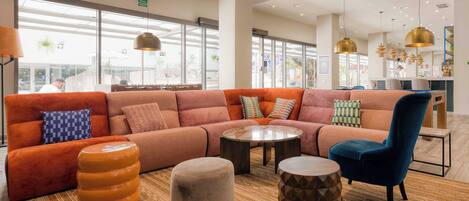 Un área de estar moderna con un sofá naranja grande, una mesa de centro redonda y un sillón azul.
