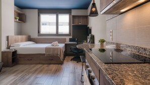A compact bedroom with a bed, bedside table, and a desk with a chair. There is a window providing natural light and a view of the outside. - Livensa Living Studios Valencia Marina Real (Valencia)