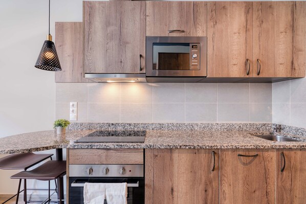 A modern kitchen with wooden cabinets, a built-in microwave, granite countertop, and a stainless steel sink. - Livensa Living Studios Valencia Marina Real (Valencia)