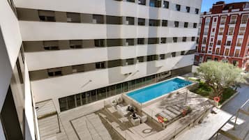 A multi-story hotel with a rooftop pool area featuring sun loungers and a small seating area.