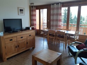 A room with a wooden cabinet, a television, a dining table with chairs, and a sofa.