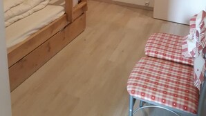 Ein Stockbett mit Holzleiter, ein kleiner Tisch mit kariertem Tuch und ein Regal mit Teddybär und Flasche.