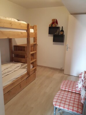 A bunk bed with a wooden ladder, a small table with a checkered tablecloth, and a shelf with a teddy bear and a bottle.