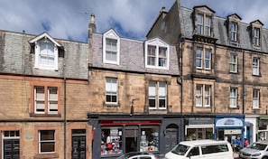 A row of traditional stone buildings with multiple stories, featuring a variety of storefronts including a British Heart Foundation Scotland charity shop and a hairdressing salon. - Balgownie - Beautiful Apartment Close to the Beach (North Berwick)