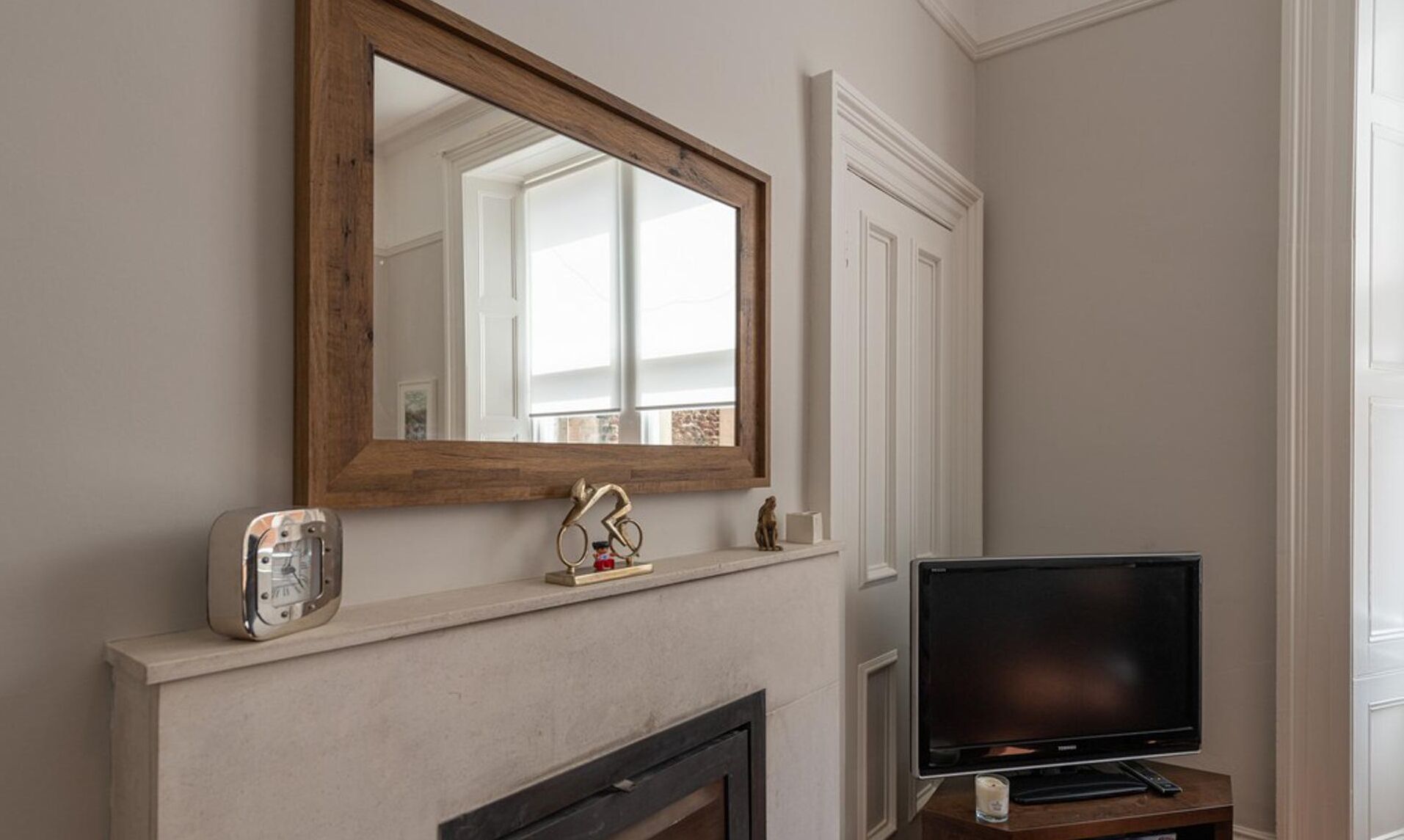 Une pièce avec une cheminée, un téléviseur posé sur un meuble et un grand miroir au-dessus du manteau de cheminée.