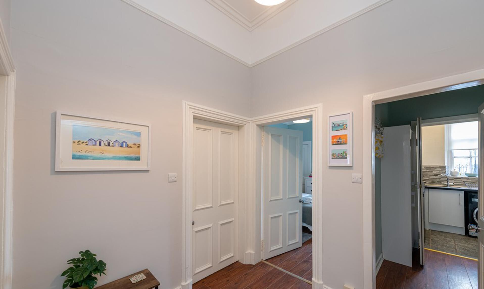 A hallway with white walls, a framed painting, and a potted plant.