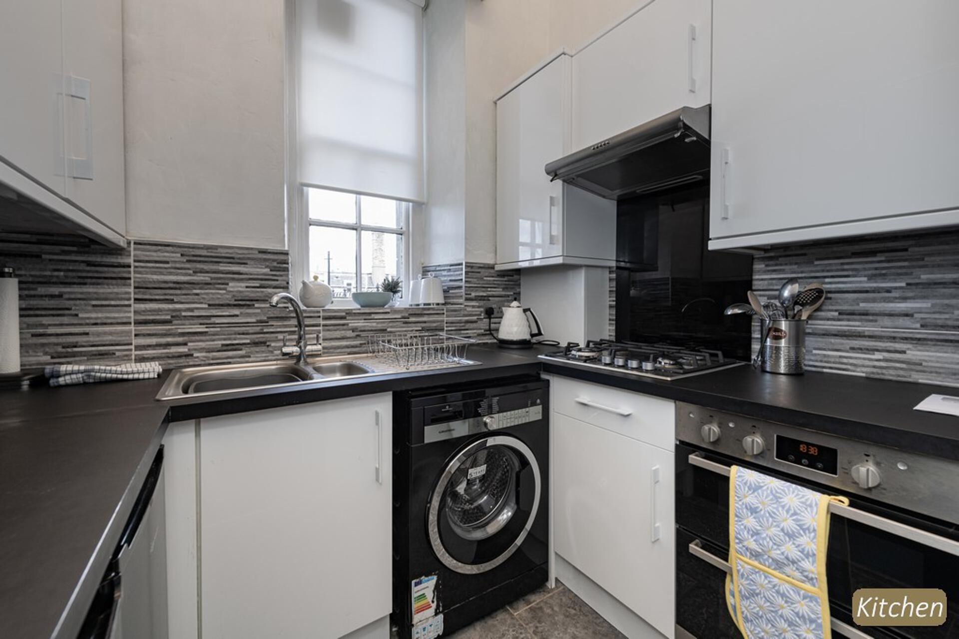 A modern kitchen with a built-in washer and dryer, stainless steel appliances, and a large window providing natural light.