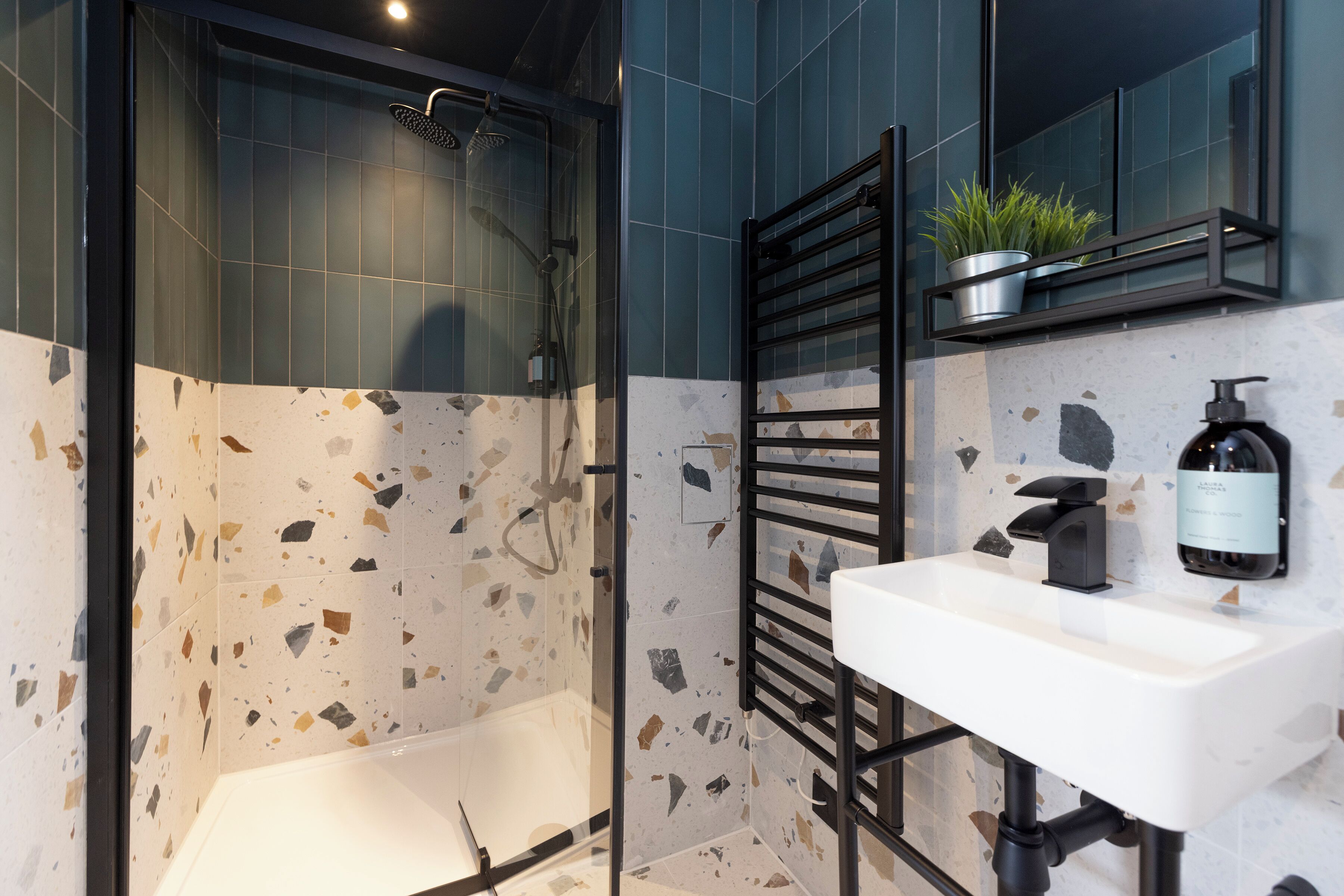 A modern bathroom with a freestanding bathtub, a glass-enclosed shower, a white sink, and a shelf with a potted plant.