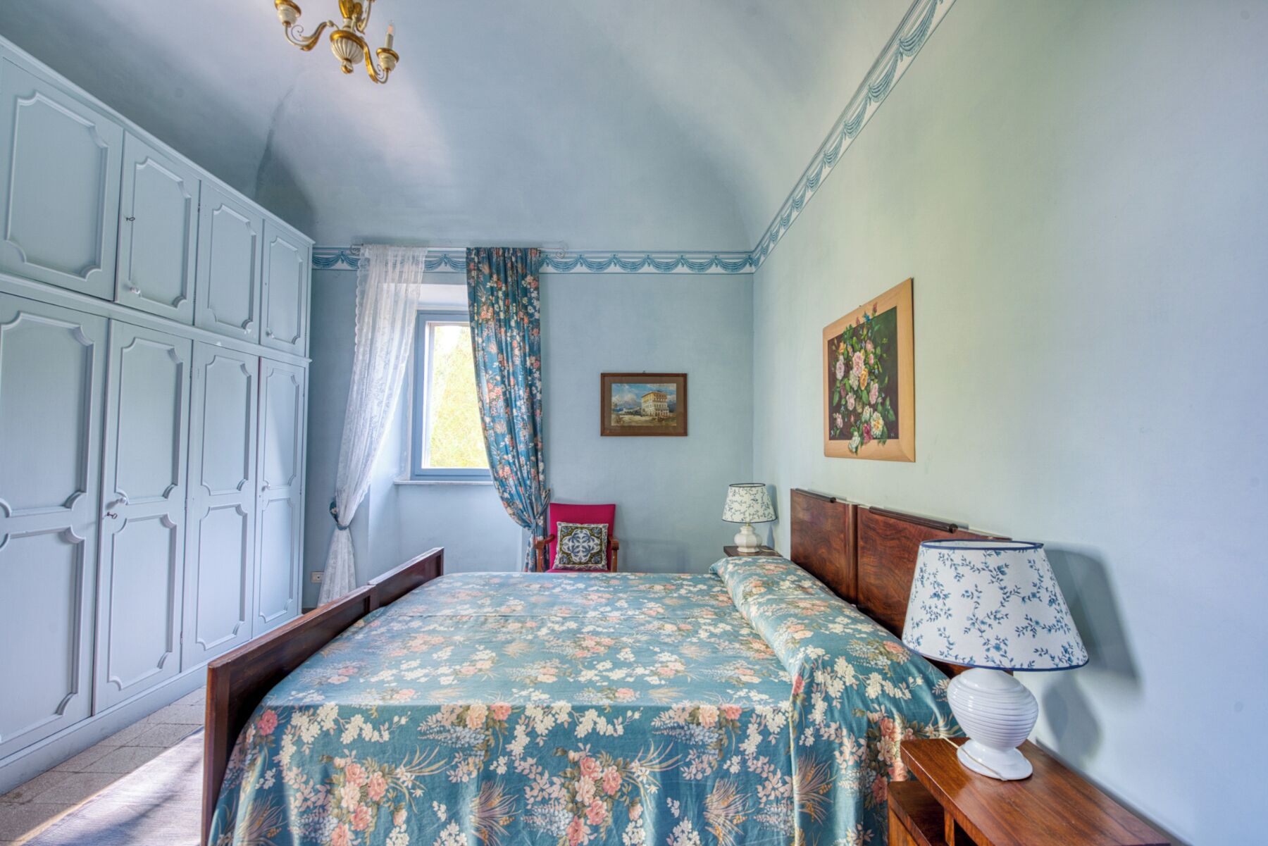 A bedroom with a bed, a nightstand, a lamp, a wardrobe, and a window with curtains.