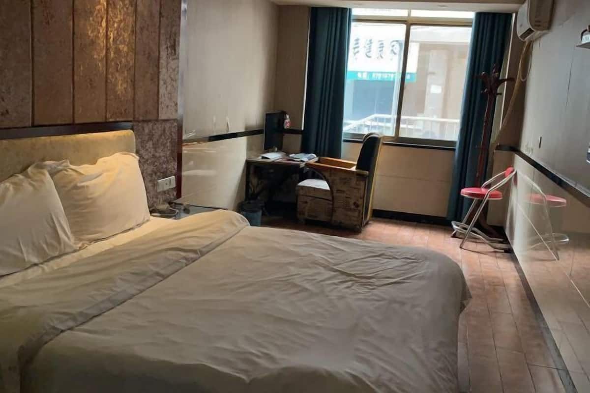 A hotel room with a bed, a desk, a chair, and a window with curtains.