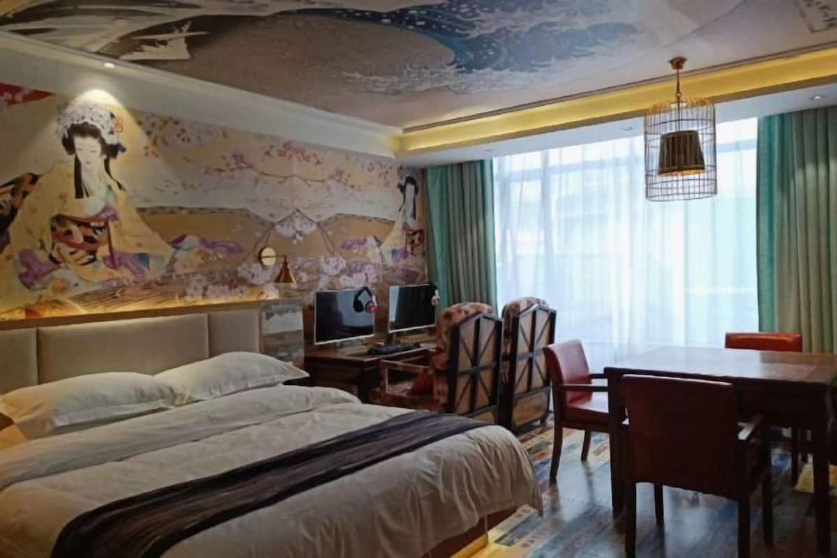 A hotel room with a large bed, a desk with a computer, a dining table with chairs, and a mural on the wall.