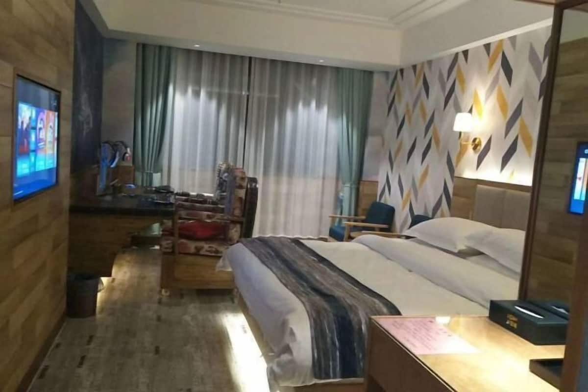 A hotel room with a bed, a desk, a chair, a TV, and a window with curtains.
