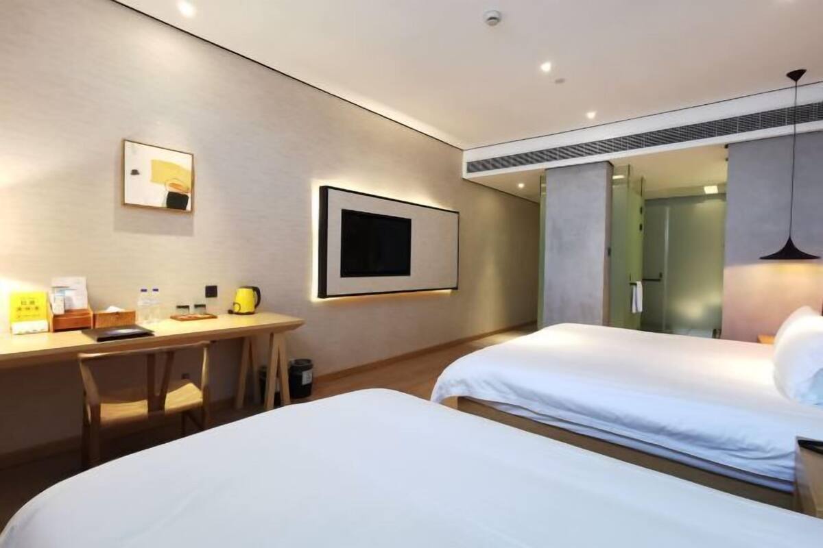 Une chambre d’hôtel moderne équipée de deux lits, d’un bureau, d’une télévision à écran plat et d’un grand miroir.