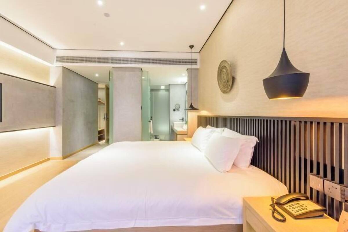 Une chambre d’hôtel moderne avec un grand lit, un téléphone sur la table de chevet et un luminaire fixé au mur.