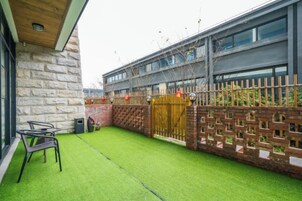 Un patio con césped artificial, valla de madera y pared de piedra.