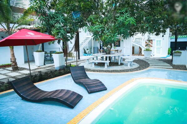 Relax by the serene pool surrounded by lush greenery and a shaded dining area.