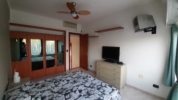 A bedroom with a bed, a TV, a wardrobe, and a ceiling fan.