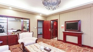 Quarto de hotel com um espelho grande, televisão, sofá, mesa de centro e chão coberto de carpete.