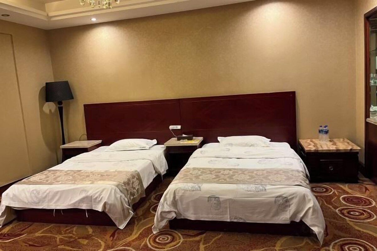A hotel room with two beds, a nightstand, a lamp, and a water bottle on the nightstand.