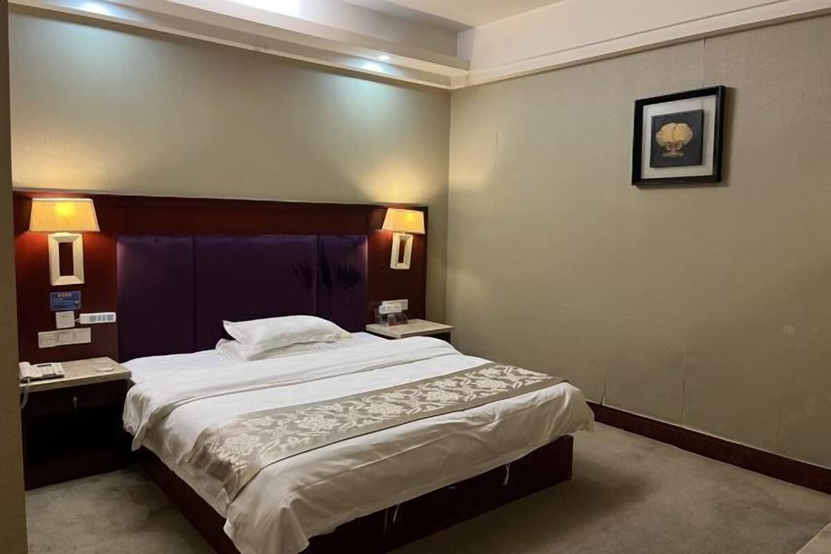 A hotel room with a large bed, two bedside tables with lamps, a framed picture on the wall, and a carpeted floor.