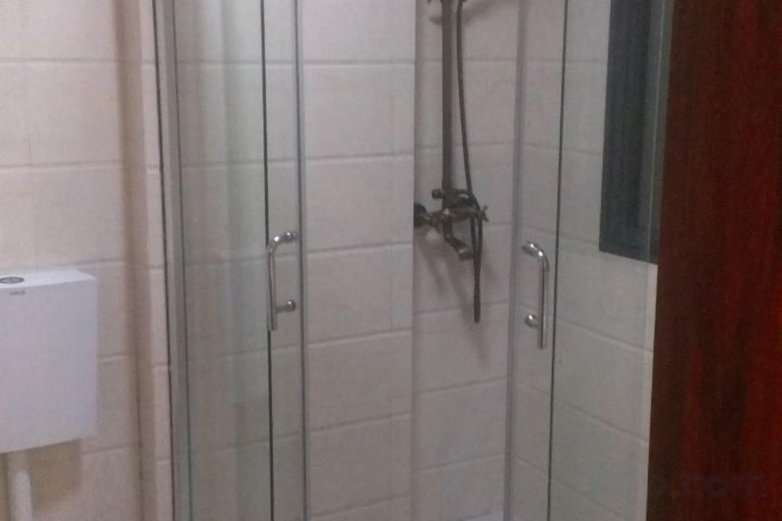 A glass-enclosed shower area with a handheld showerhead and a control panel on the wall.