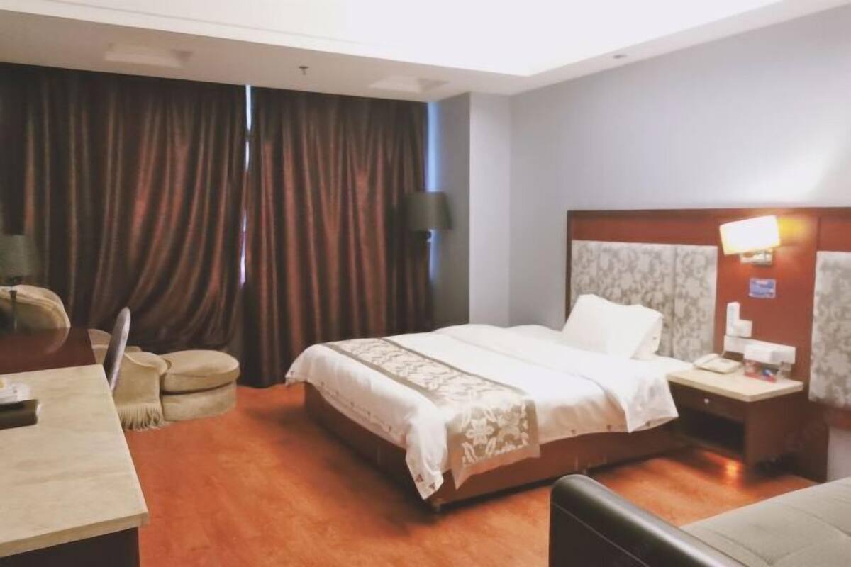 A hotel room with a bed, bedside table, lamp, and a desk with a chair.