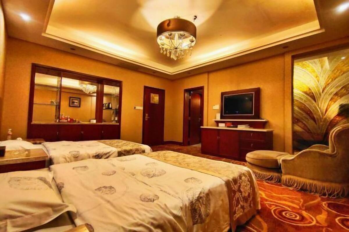 A hotel room with two beds, a television, a mirror, and a chandelier.