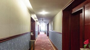 Corredor de hotel com carpete vermelho, portas de madeira e luminária no teto.