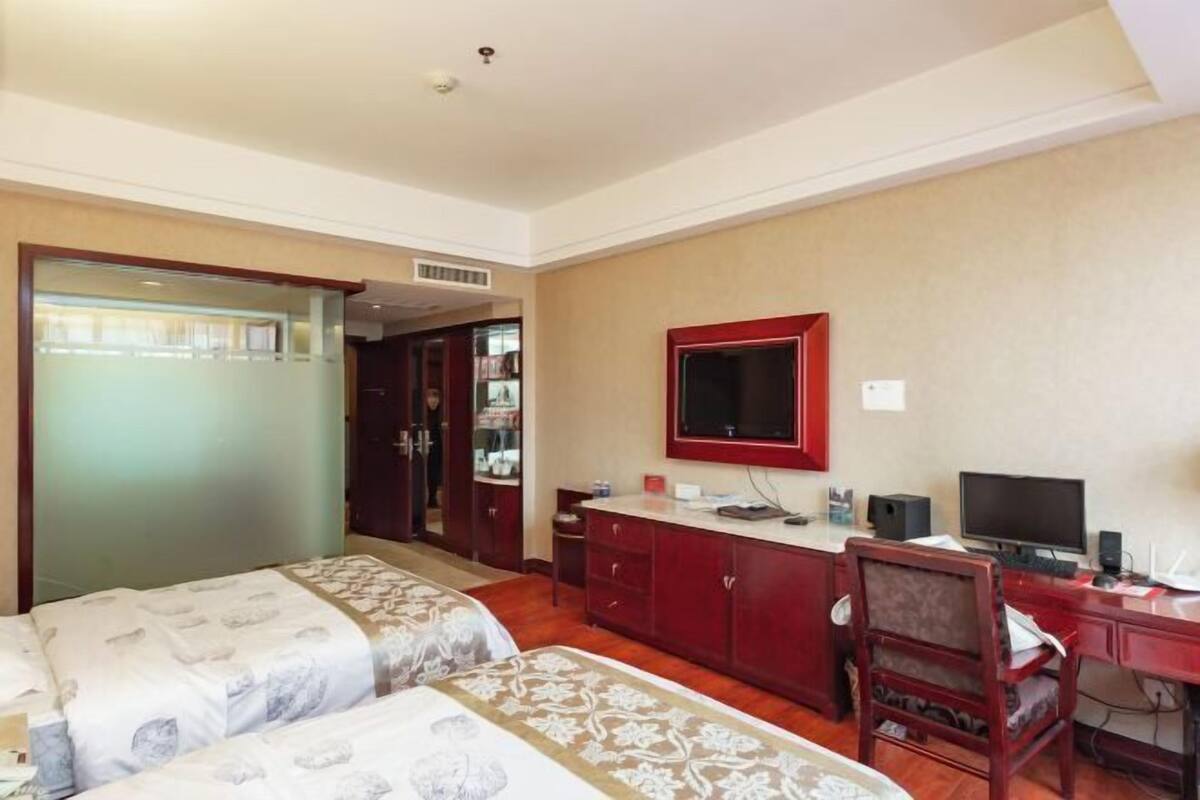 A hotel room with two beds, a desk with a computer, a mirror, and a wardrobe.