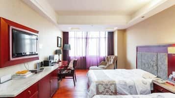 A hotel room with a TV, desk, chair, two beds, and a window with curtains.