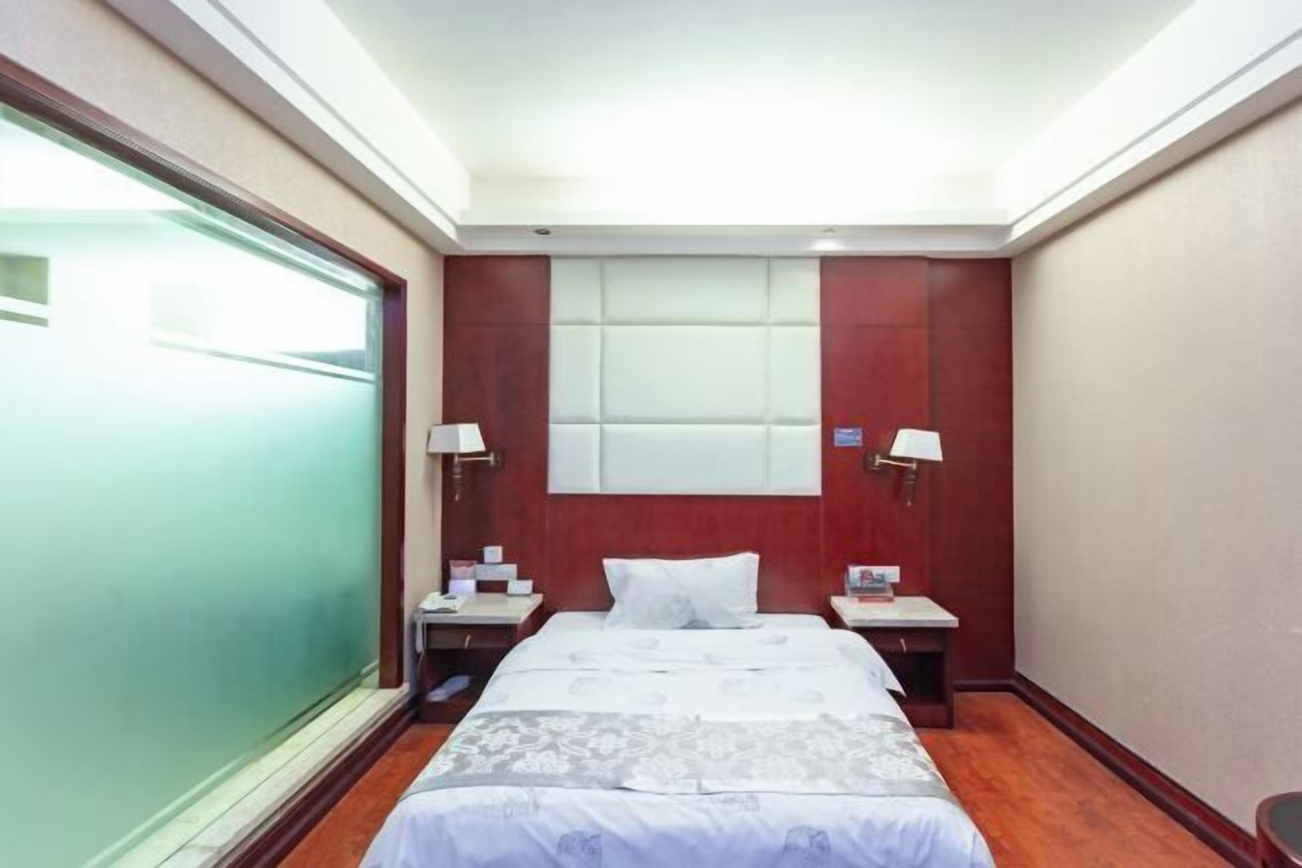 A hotel room with a bed, bedside tables, lamps, a window, and a wall-mounted light fixture.