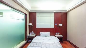 A hotel room with a bed, bedside tables, lamps, a window, and a wall-mounted light fixture.