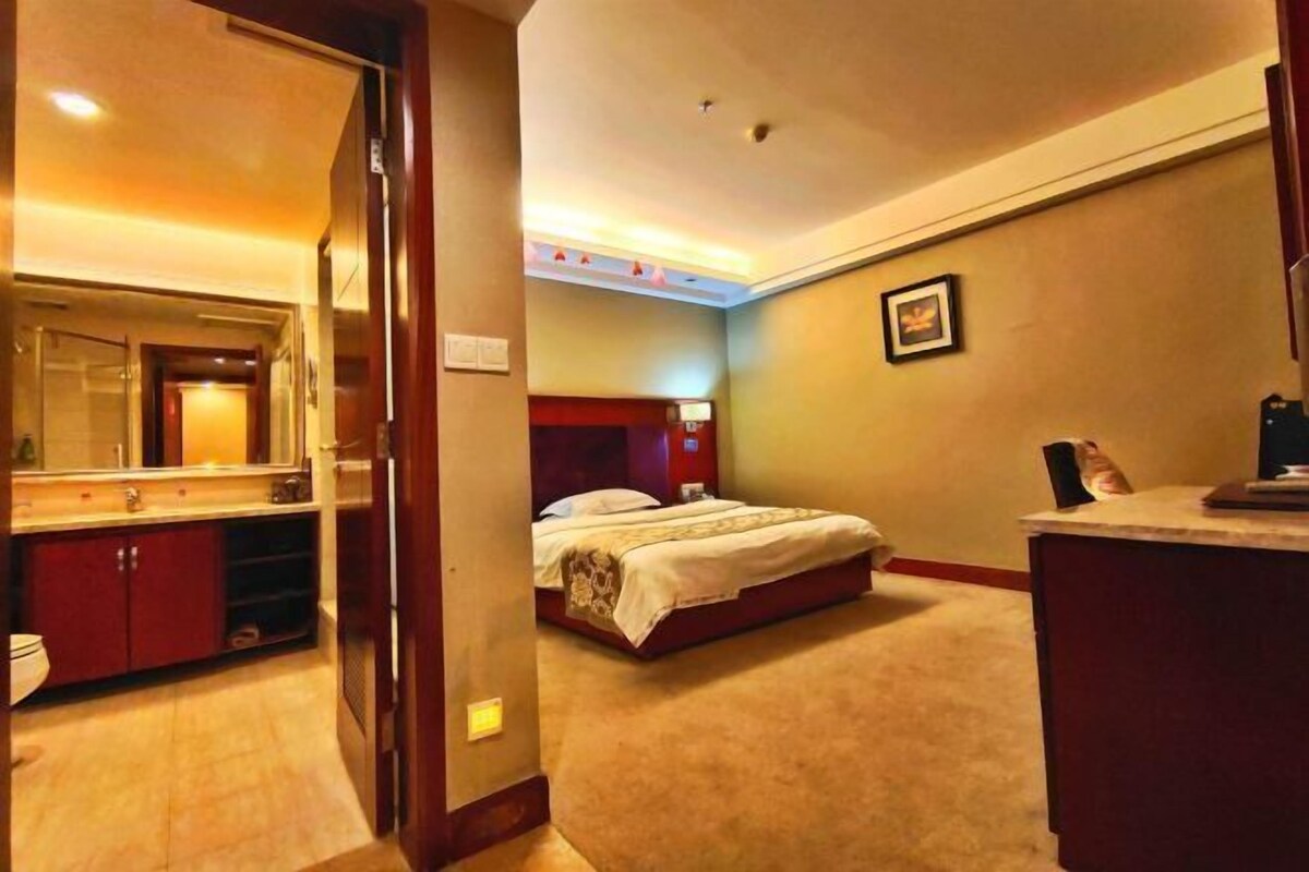 A hotel room with a bed, a bedside table, a desk, a chair, a mirror, and a bathroom with a toilet and sink.