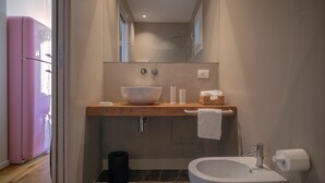 A bathroom with a wooden vanity, a large vessel sink, a toilet, and a trash can. - WeLive Trapani - Deluxe First Floor Apartment (Trapani)