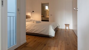 A bedroom with a bed, a nightstand, a lamp, a small wooden stool, and a door leading to a balcony. - WeLive Trapani - Penthouse apartment with terrace and Jacuzzi (Trapani)