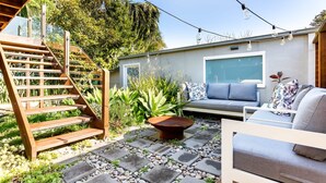 A patio with a wooden staircase, a seating area with cushions, and a fire pit.